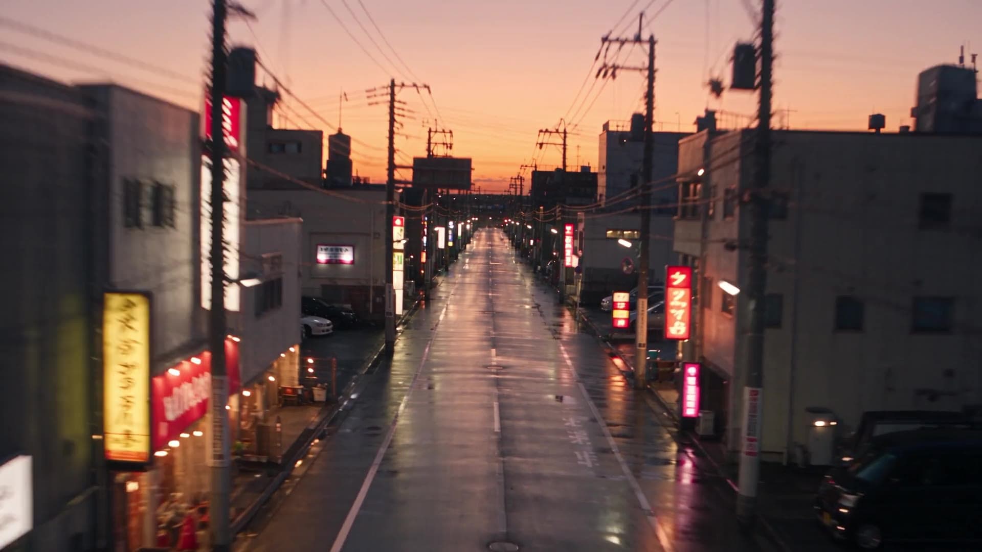 A rain-slicked street at dusk, lined with glowing signs