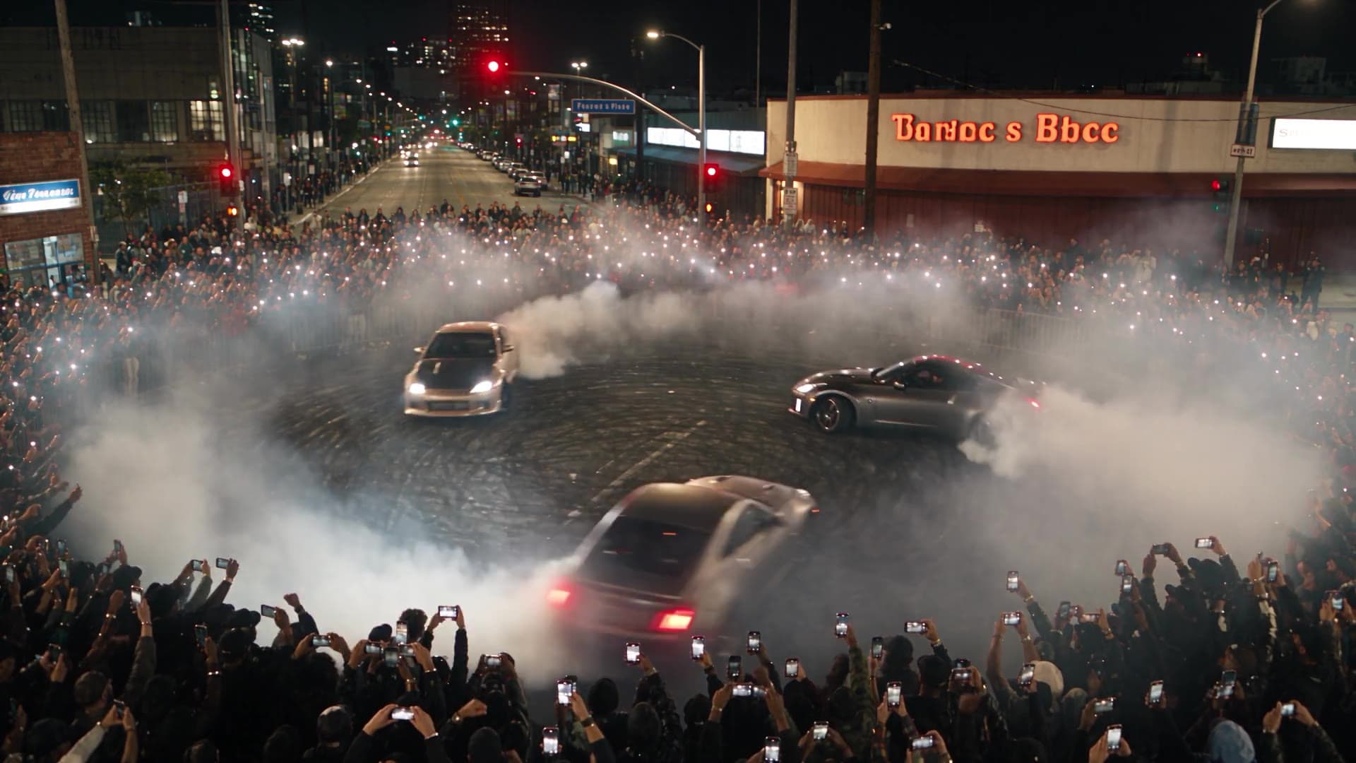 Two cars drifting through a crowd at night, wrapped in smoke