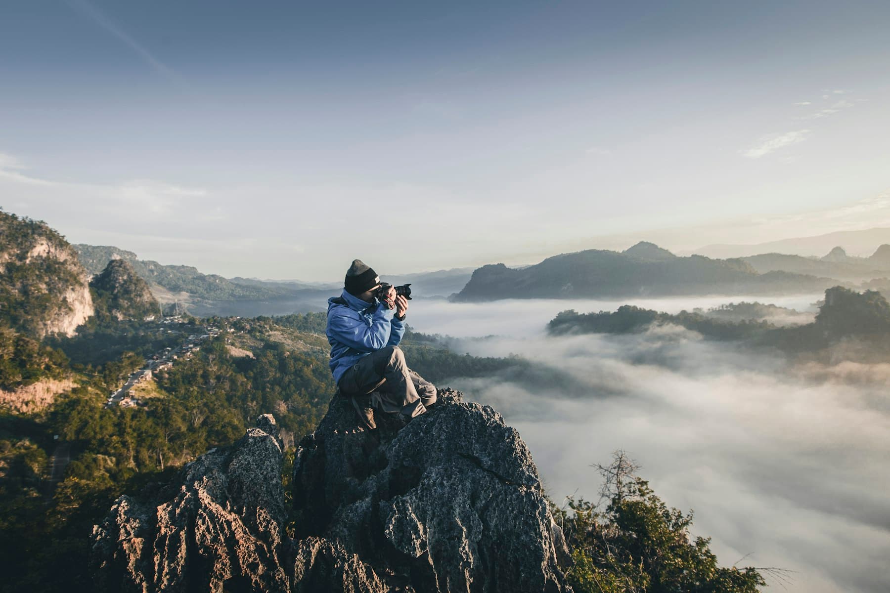 A photographer crouched on a rocky peak above a valley of clouds